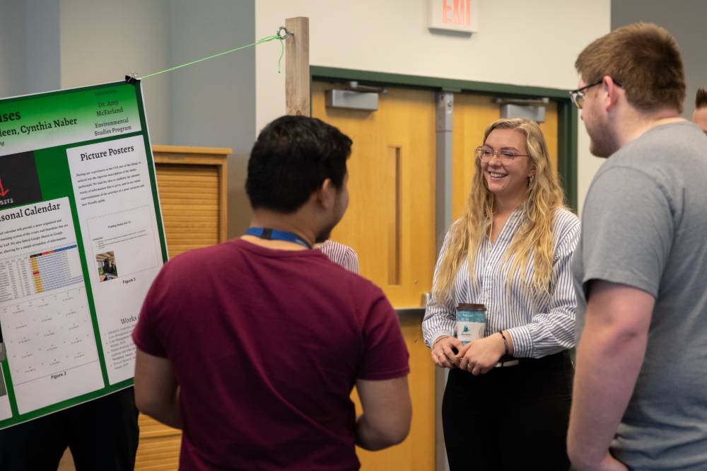 Three students smile while talking about a poster presentation